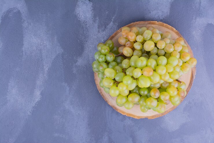 Foto gratuito uvas verdes en un plato de madera sobre superficie azul
