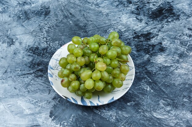 Uvas verdes en un plato sobre un fondo de yeso sucio. vista de ángulo alto.