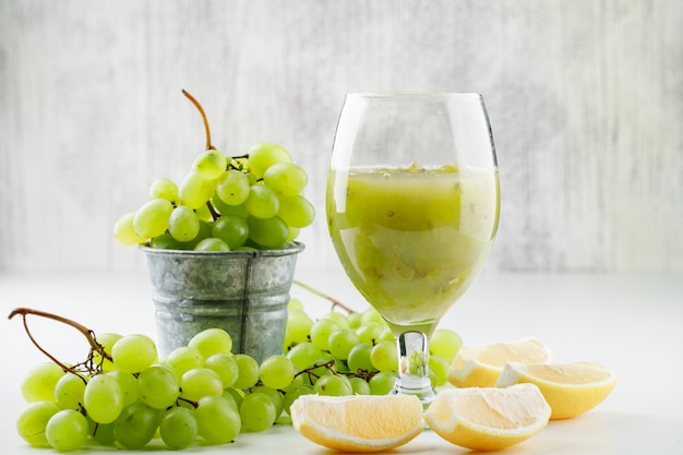 Uvas verdes con rodajas de limón, cóctel de uva en un mini cubo sobre superficie blanca