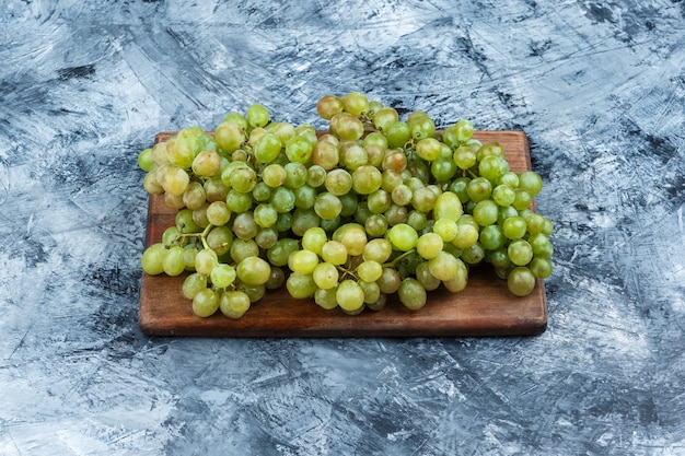 Uvas verdes sobre fondo gris sucio y tabla de cortar. horizontal