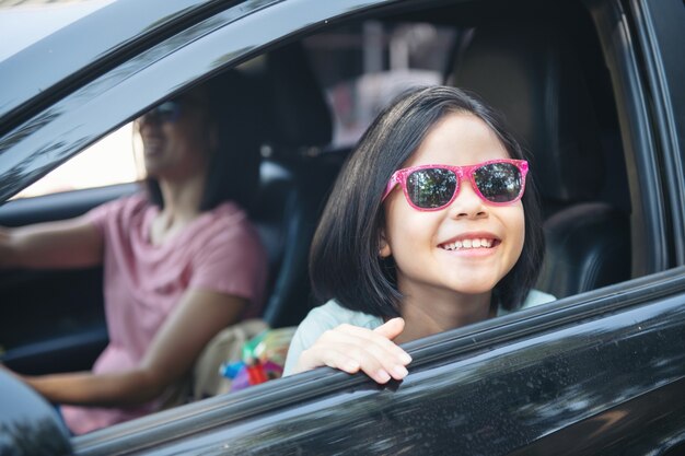 Vacaciones familiares, familia feliz en un viaje por carretera en su automóvil, mamá conduciendo un automóvil mientras su hija está sentada al lado, mamá e hija están viajando. Paseo de verano en automóvil.