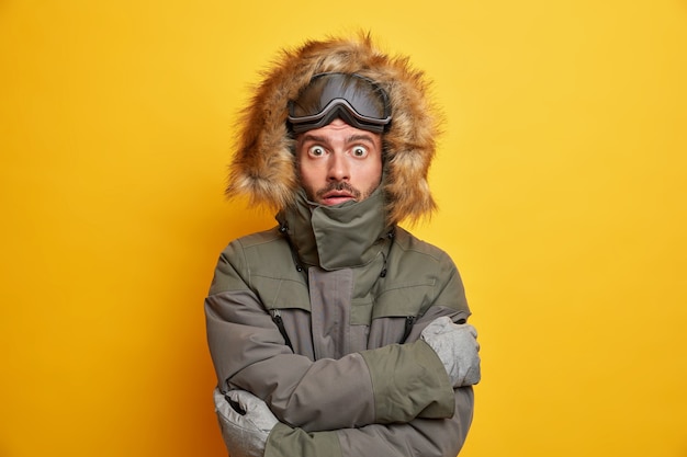 Vacaciones de invierno y concepto de deporte extremo. Snowboarder conmocionado tiembla de frío se abraza a sí mismo mientras trata de calentarse durante el día helado en la estación de esquí de montaña.