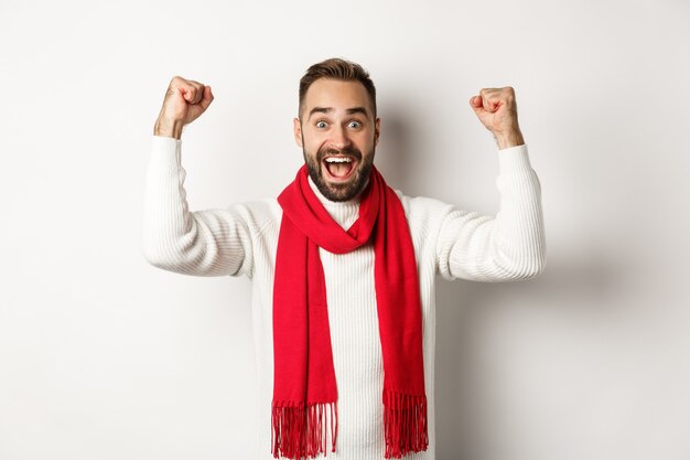 Vacaciones de Navidad y concepto de año nuevo. Hombre emocionado regocijándose, ganando el premio, levantando las manos y luciendo aliviado, triunfando, de pie sobre fondo blanco.