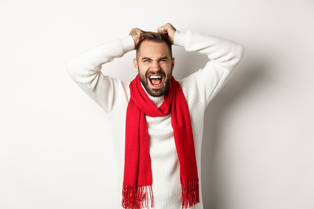 Vacaciones de Navidad y concepto de año nuevo. Hombre frustrado y enojado quitándose el cabello de la cabeza y gritando angustiado, de pie enojado contra el fondo blanco.