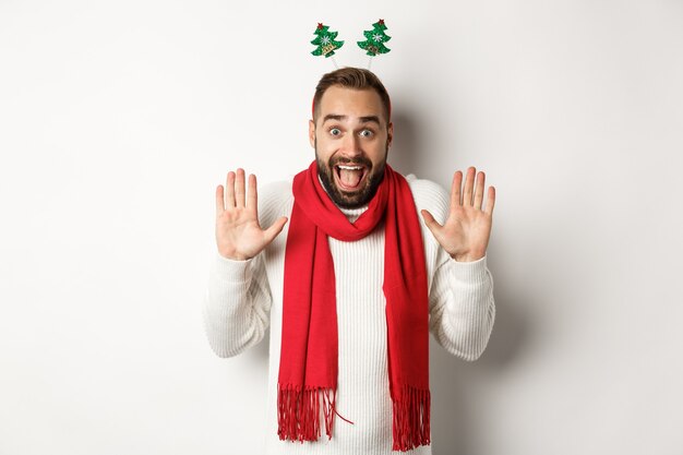 Vacaciones navideñas. Hombre barbudo emocionado levantando las manos y gritando de alegría, celebrando la fiesta de Año Nuevo, de pie contra el fondo blanco.