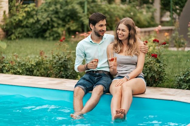 Vacaciones de verano, gente, romance, concepto de citas, pareja bebiendo vino espumoso mientras disfruta del tiempo juntos sentados en la piscina