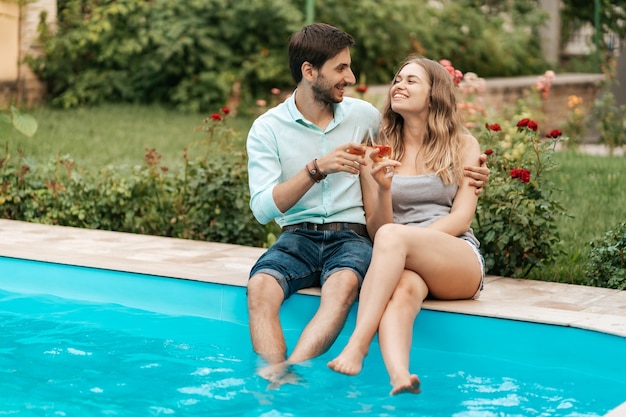 Vacaciones de verano, gente, romance, concepto de citas, pareja bebiendo vino espumoso mientras disfruta del tiempo juntos sentados en la piscina