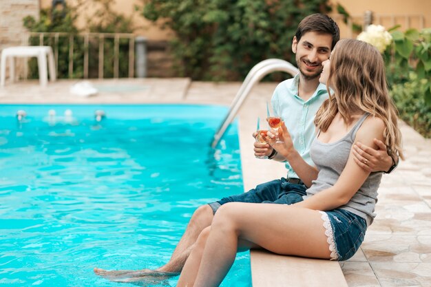 Vacaciones de verano, gente, romance, concepto de citas, pareja bebiendo vino espumoso mientras disfruta del tiempo juntos sentados en la piscina