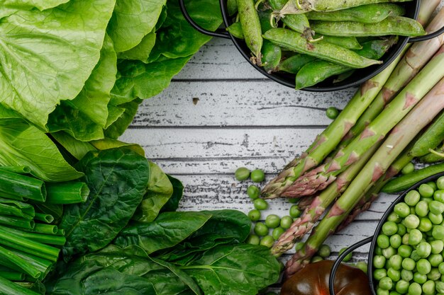 Vainas verdes, guisantes con tomate, acedera, espárragos, cebolla verde, lechuga en cacerolas en la pared de madera, endecha plana.