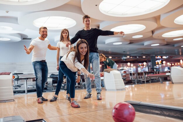 Vamos, puedes hacerlo. Jóvenes amigos alegres se divierten en el club de bolos en sus fines de semana