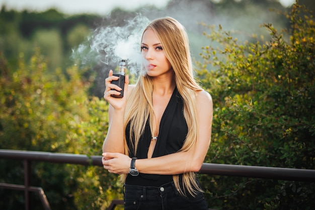 Vaping. Mujer hermosa joven que fuma el e-cigarrillo con humo al aire libre.