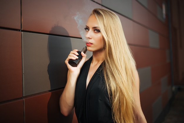 Vaping. Mujer hermosa joven que fuma el e-cigarrillo con humo al aire libre.