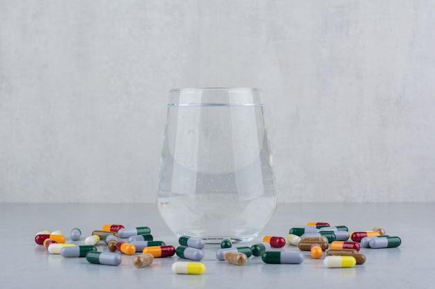 Varias cápsulas farmacéuticas y vaso de agua.