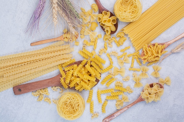 Varias formas de pasta cruda y cucharas en espacios en blanco.