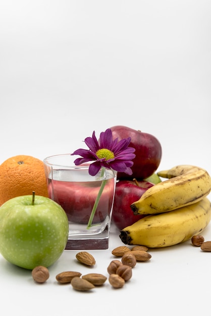 Varias frutas; avellana; Almendra con vaso de agua y flor en fondo blanco