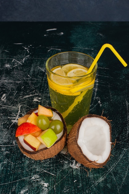 Varias frutas en la mitad de coco cortado y un vaso de jugo en la mesa de mármol