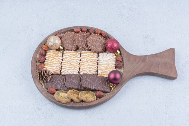 Varias galletas, frutos secos y bolas de Navidad sobre tabla de madera.