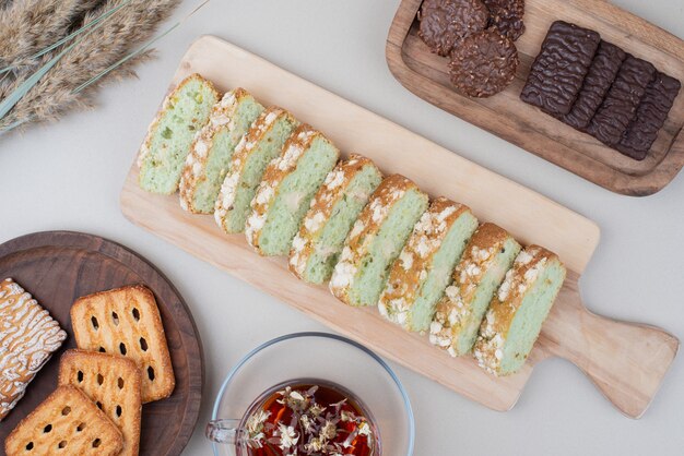 Varias galletas, rebanadas de pastel y taza de té en blanco.