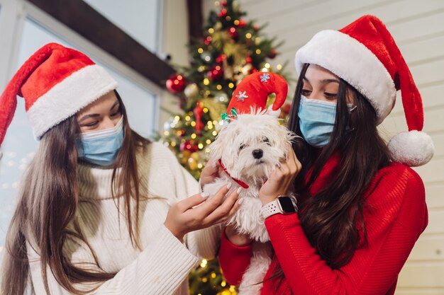 Varias niñas juegan con un perro pequeño en la víspera de Año Nuevo en casa. Navidad durante el coronavirus, concepto