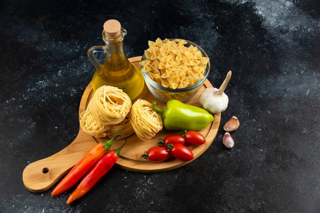 Varias pastas, aceite y verduras sobre tabla de madera.