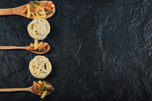 Foto gratuita varias pastas sin cocer en cucharas de madera sobre la oscuridad.