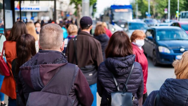 Varias personas esperando el transporte en una estación, automóviles en la carretera.