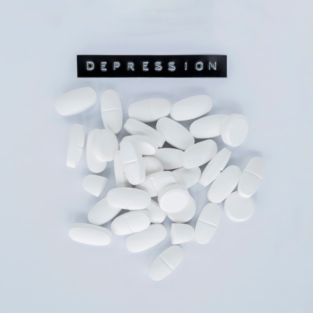 Varias píldoras blancas con etiqueta de depresión sobre fondo gris