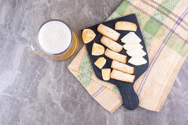 Varias rodajas de queso y limón en tablero oscuro con cerveza. Foto de alta calidad