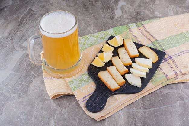 Varias rodajas de queso y limón en tablero oscuro con cerveza. Foto de alta calidad