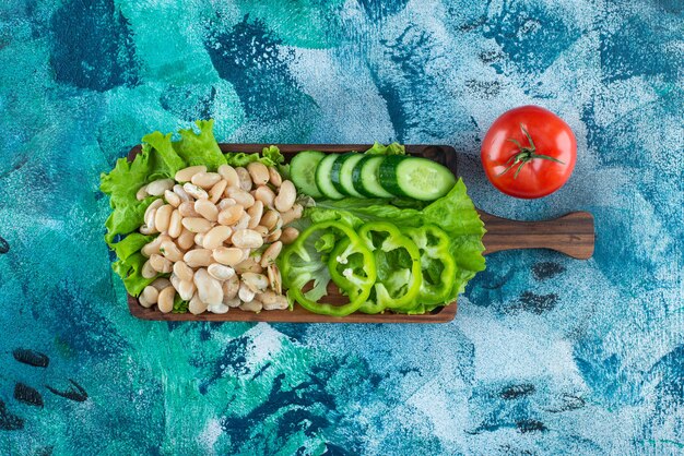 Varias verduras y frijoles en un tablero sobre la mesa azul.