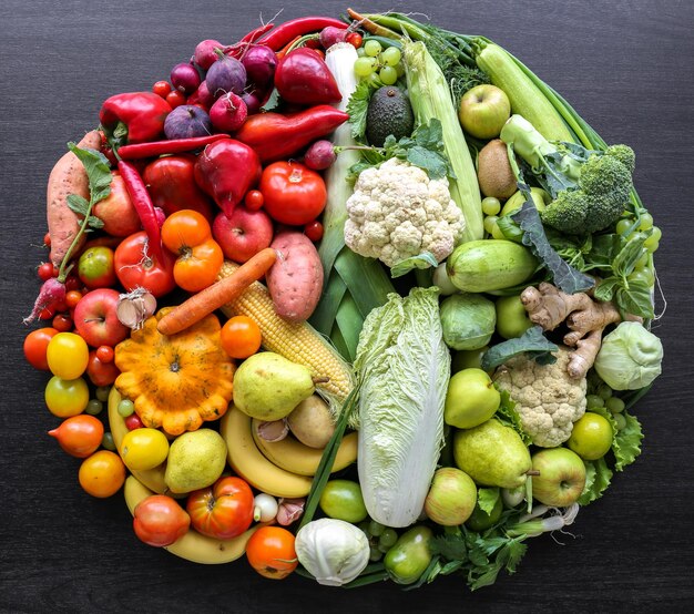 Varias verduras y frutas dispuestas en círculo sobre un fondo oscuro