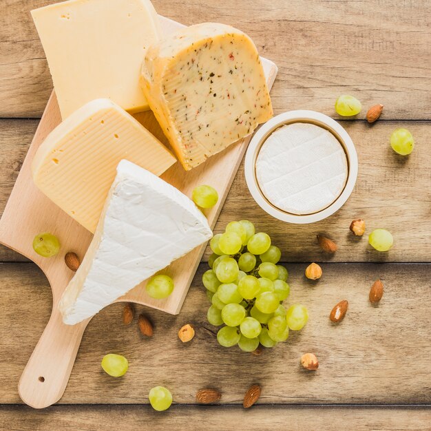 Variedad de bloques de queso con uvas; Almendras y castañas sobre mesa de madera.