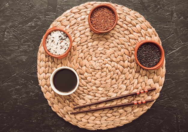 Variedad de granos de arroz en tres cuencos sobre el mantel circular con palillos