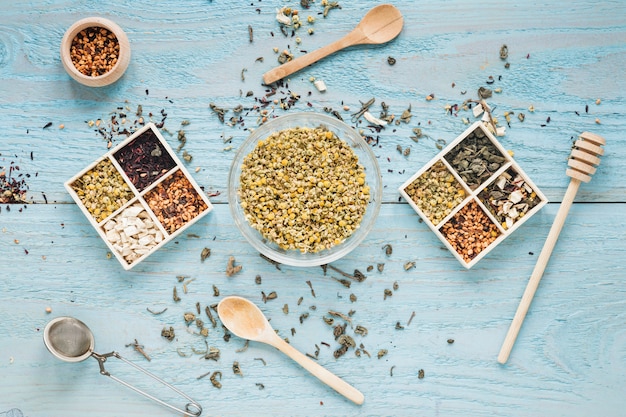 Foto gratuita variedad de hierbas; cuchara; cucharón de miel; el colador de té y las flores secas de crisantemo chino arreglan en la mesa
