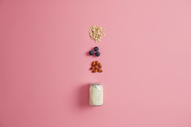 Foto gratuita variedad de ingredientes saludables para un desayuno saludable. yogur, cereales de avena, arándano, nuez de almendra para mezclar sobre fondo rosa. productos deliciosos para preparar deliciosas papillas nutritivas. concepto de alimentación