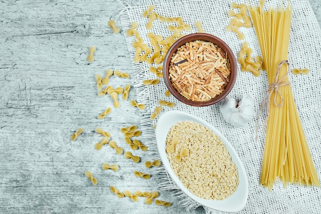 Variedad de pasta cruda con ajo y mantel blanco.