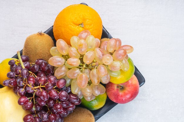 Variedad de sabrosas frutas en bandeja negra, sobre el mármol.