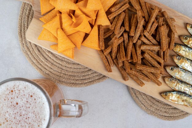 Variedad de snacks en tablero de madera con vaso de cerveza.