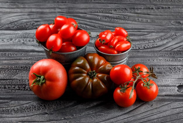 Variedad de tomates en mini cubos en la pared de madera gris, vista de ángulo alto.