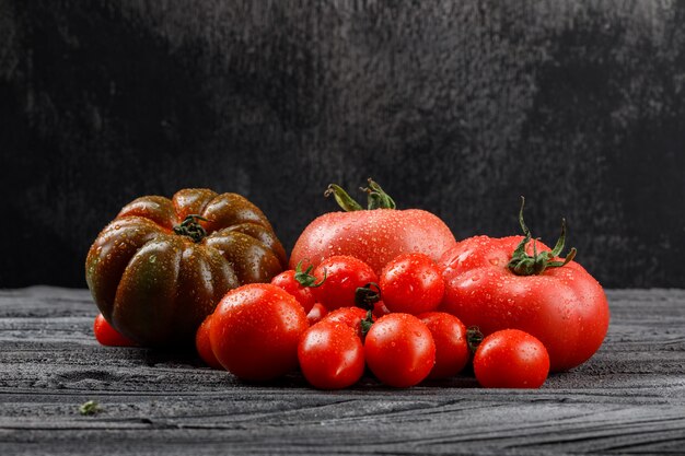 Variedad de tomates en la pared de madera y oscura, vista lateral.