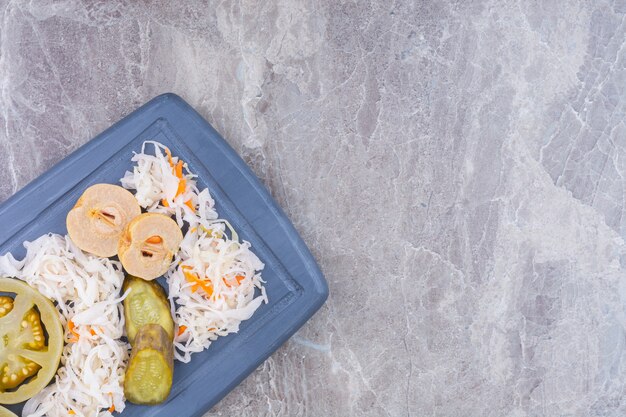 Una variedad de verduras en escabeche en una bandeja de madera, sobre el mármol.