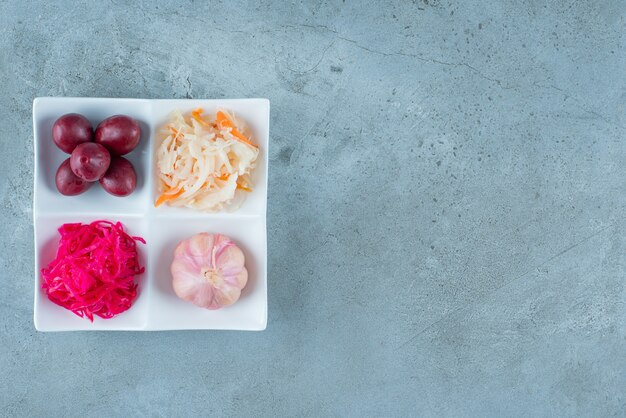 Una variedad de verduras fermentadas en un plato, sobre la mesa de mármol.