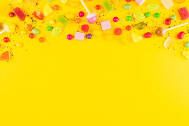 Variedades de dulces dulces coloridos en superficie amarilla.