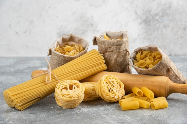 Variedades de pasta en canasta rústica con madera rosa rodante sobre mesa de mármol.