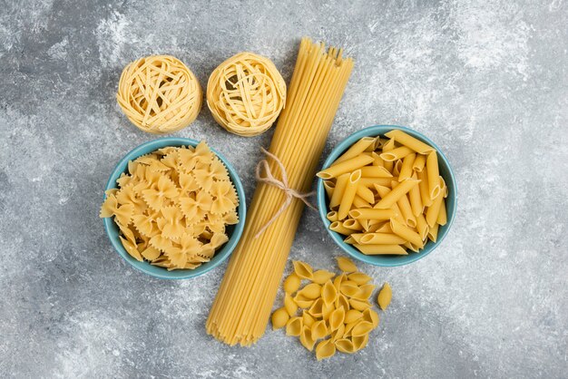 Variedades de pasta cruda y espaguetis en mesa de mármol.