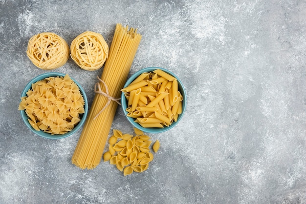 Variedades de pasta cruda y espaguetis en mesa de mármol.