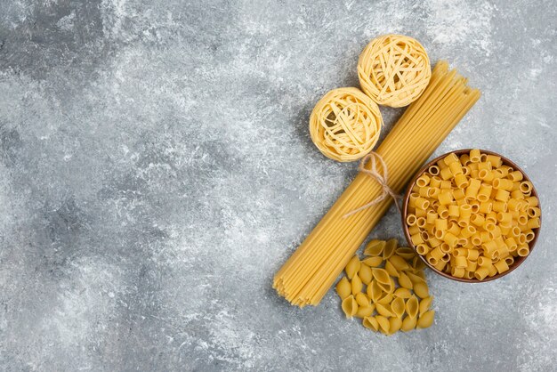 Foto gratuita variedades de pasta cruda y espaguetis en mesa de mármol.