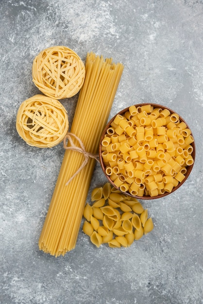 Variedades de pasta cruda y espaguetis en mesa de mármol.