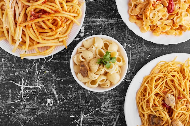 Variedades de pasta en salsa de tomate en un plato blanco sobre fondo negro.