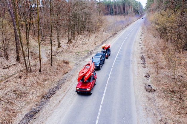 Varios autos con kayaks en la baca conduciendo en la carretera entre árboles